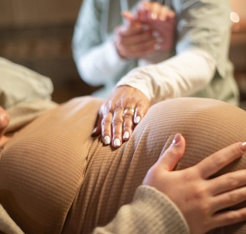 Cropped image of smiling pregnant woman and midwife at home. Woman in casual clothes lying on bed, midwife holding hand. Pregnancy, medicine, home birth concept