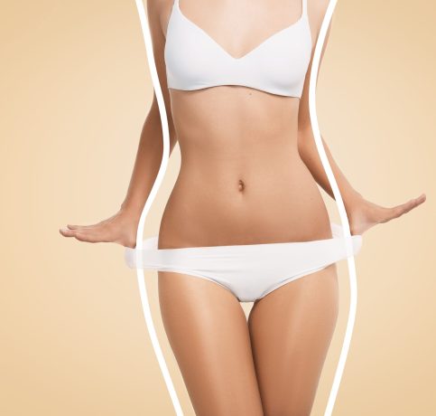 Cropped shot of slim and fit female model in white lingerie posing isolated against blank studio wall background. Close up portrait of attractive girl with perfect body wearing white bra and panties