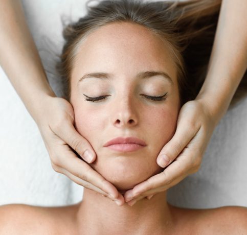 Young blond woman receiving a head massage in a spa center with eyes closed. Female patient is receiving treatment by professional therapist.