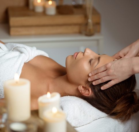 Young beautiful brunette girl having face massage relaxing in spa salon. Eyes closed. Copy space.